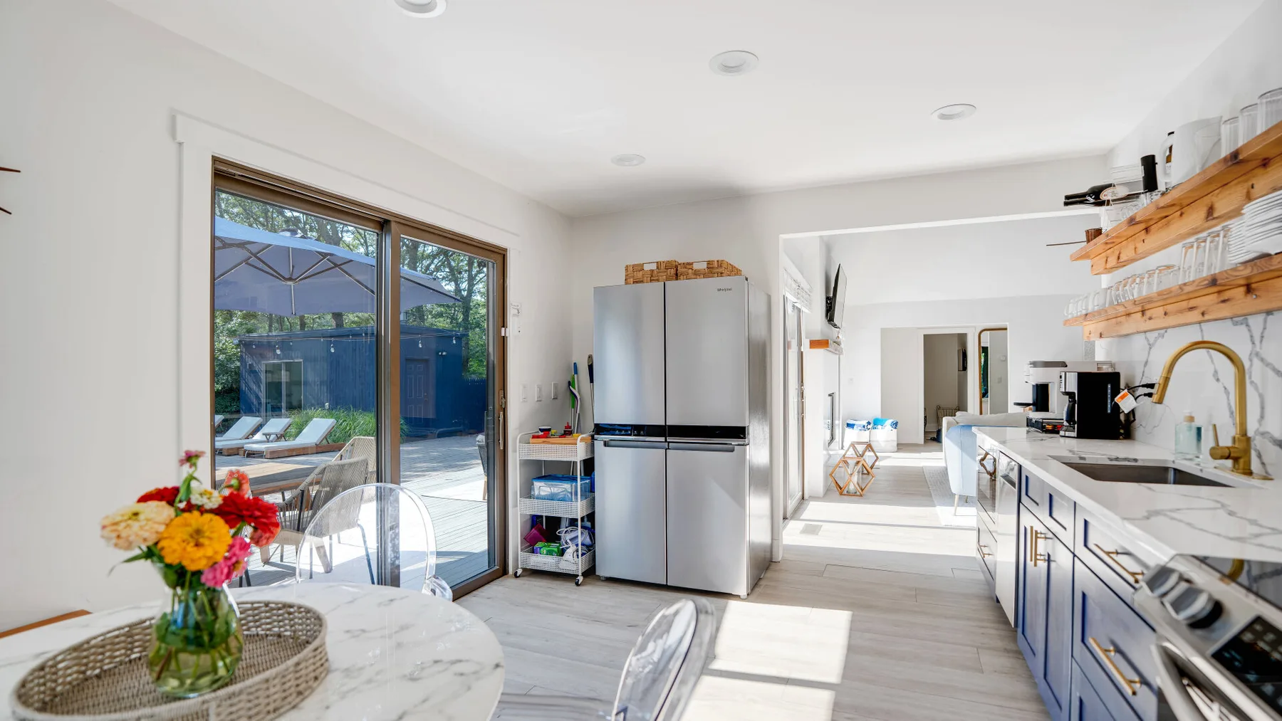 Una cocina luminosa con mesa de comedor, refrigerador de acero inoxidable y puertas corredizas de vidrio.