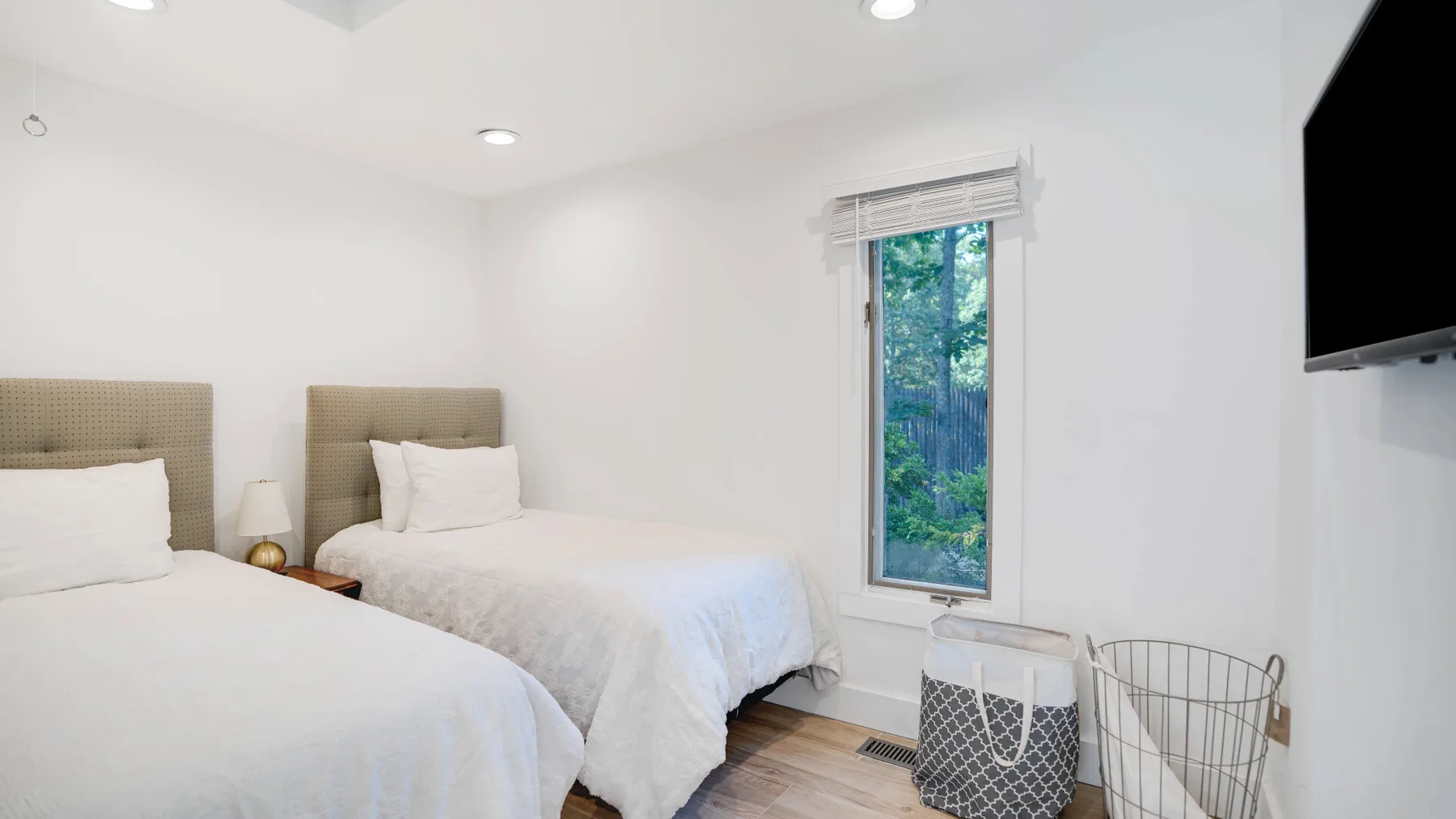 Un dormitorio luminoso con dos camas y una ventana con vista a la vegetación.