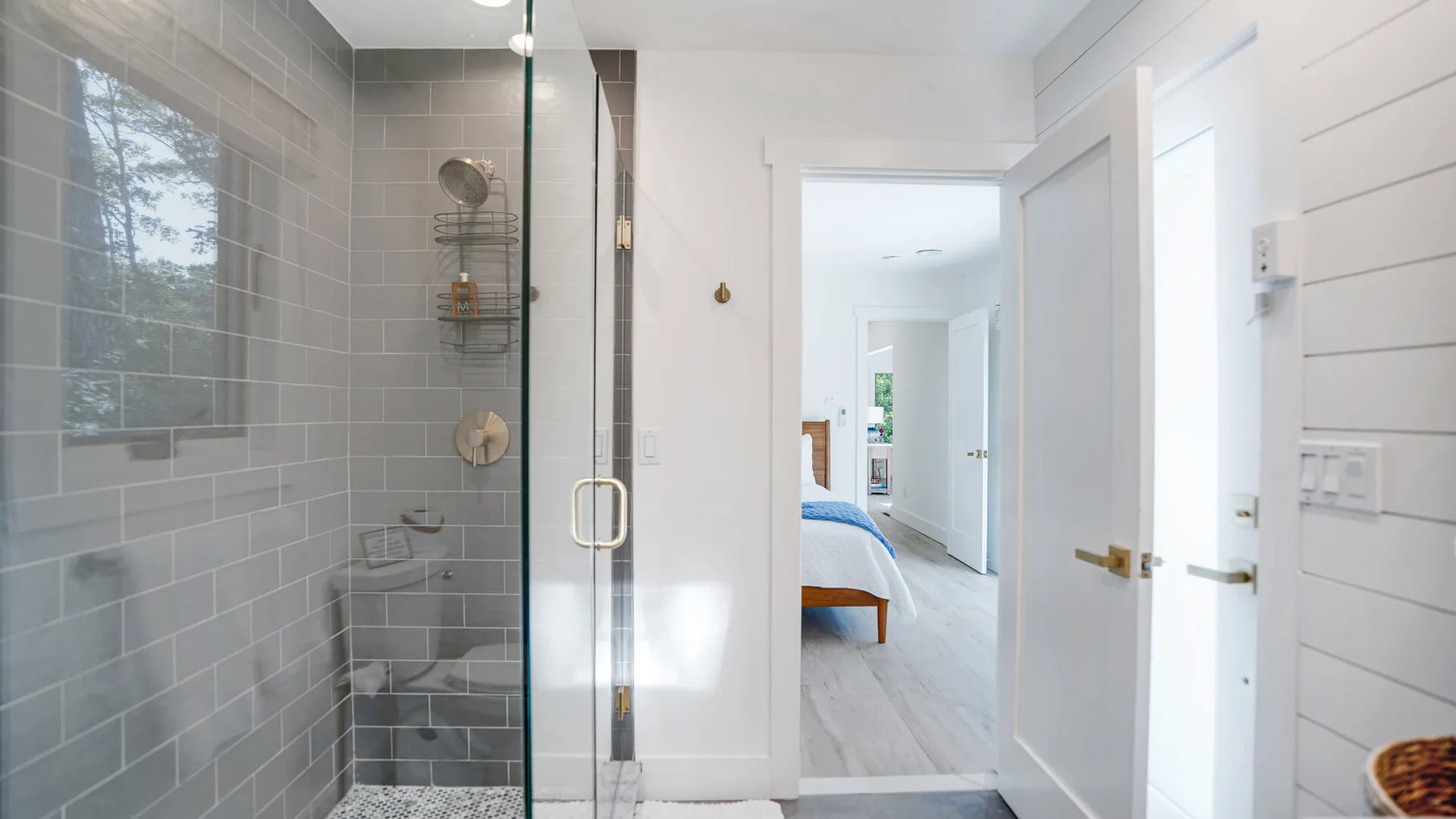Un baño luminoso con una ducha de vidrio y una puerta abierta a un dormitorio.