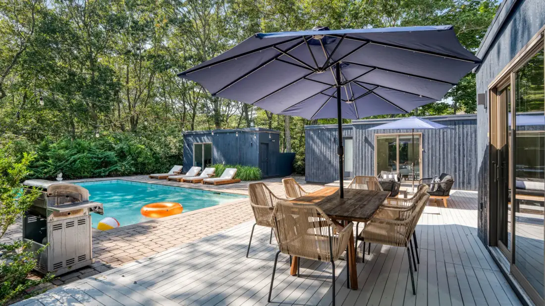 Un patio con piscina, asientos y una gran sombrilla.