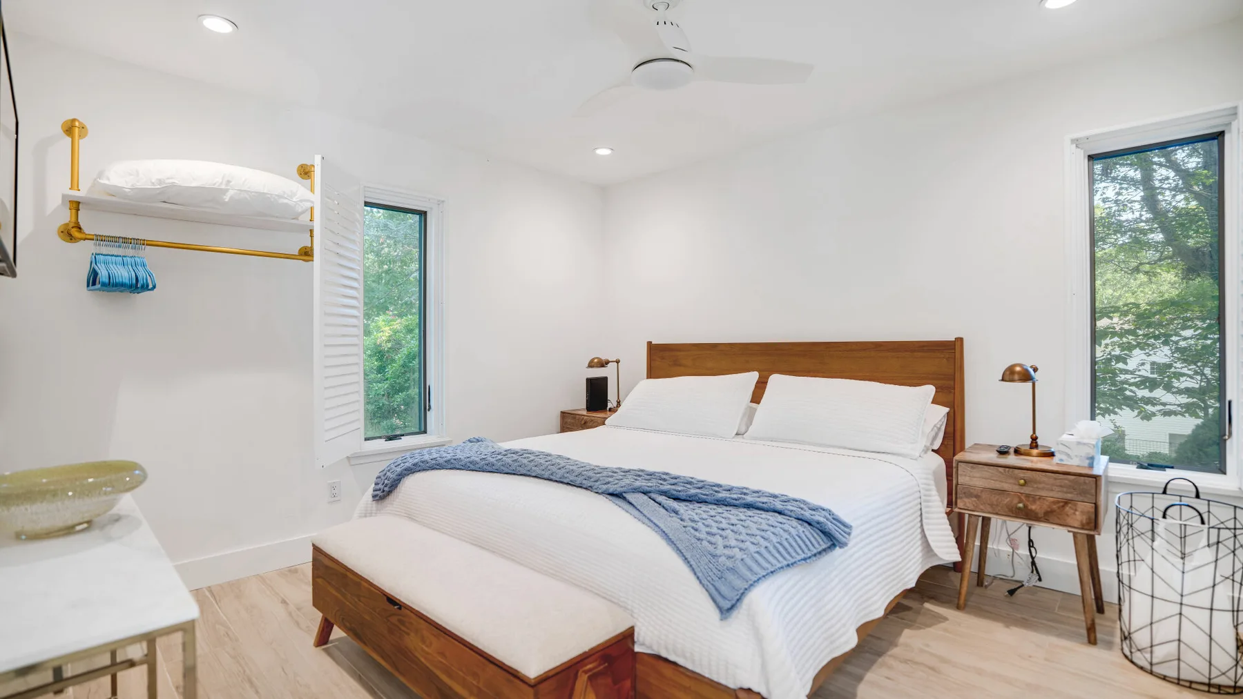 Un dormitorio luminoso con una cama, mesas de noche y grandes ventanas.