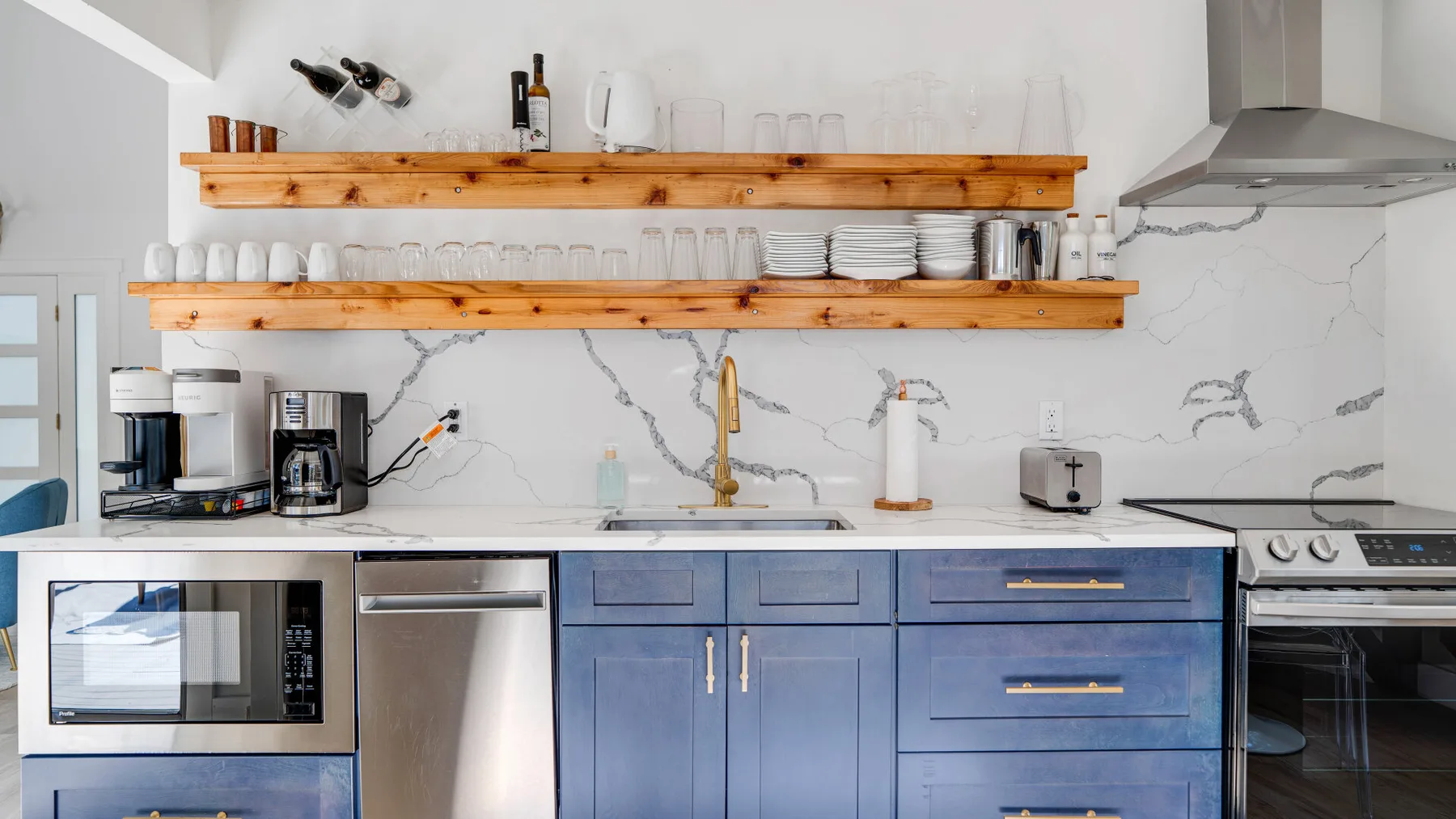 Una cocina moderna con gabinetes azules, estantes de madera abiertos y electrodomésticos de acero inoxidable.