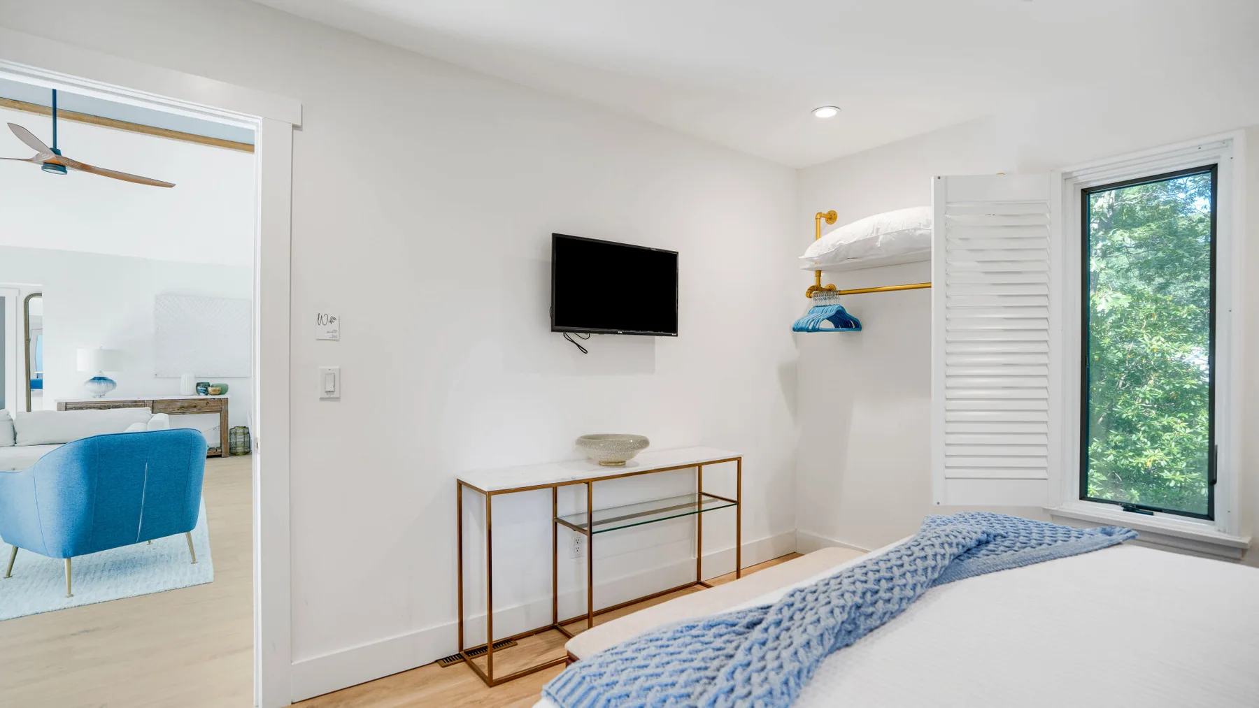 Un dormitorio luminoso con cama, televisor en la pared y armario abierto.