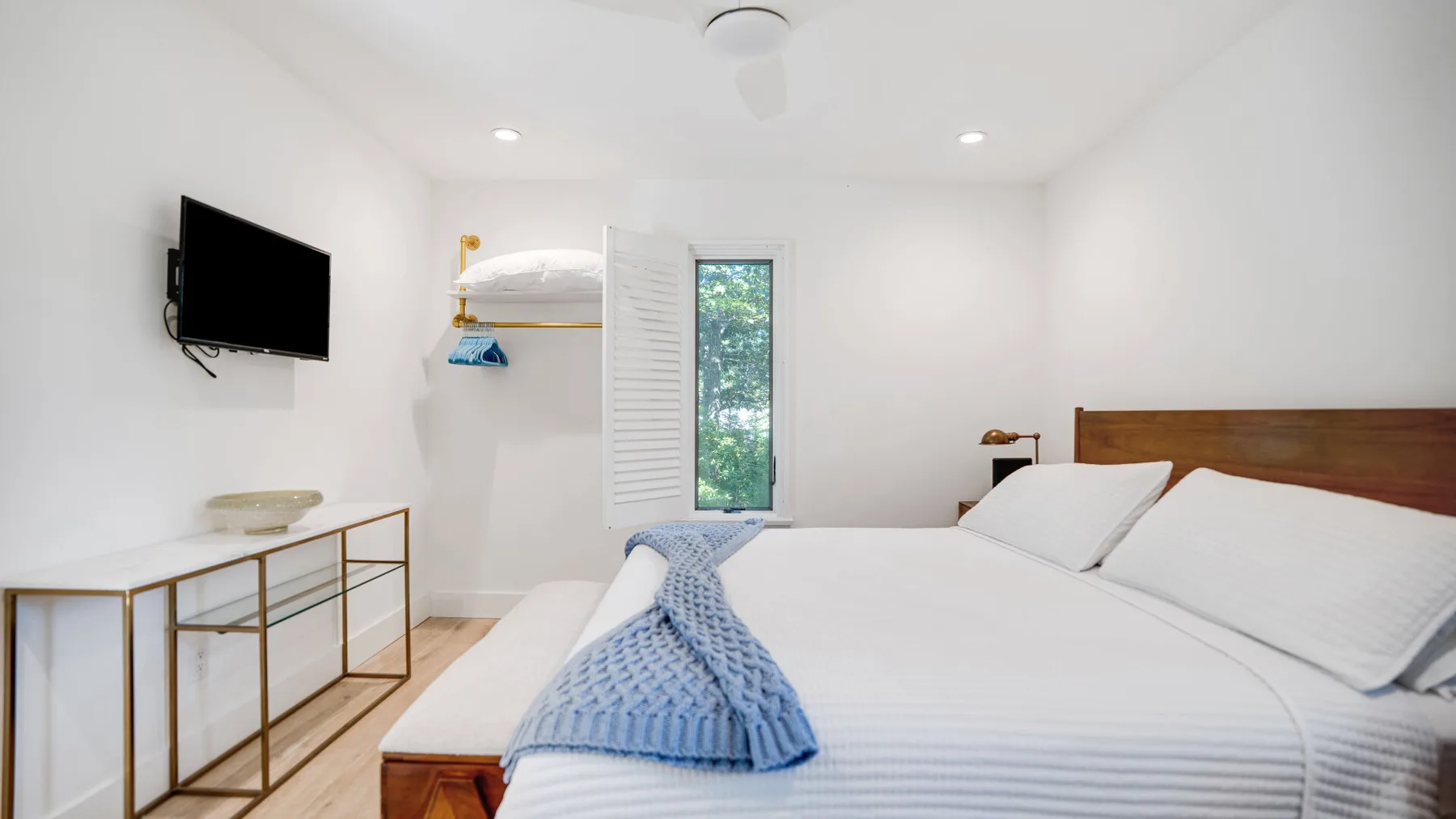 Un dormitorio luminoso con una cama, un televisor en la pared y un armario abierto.