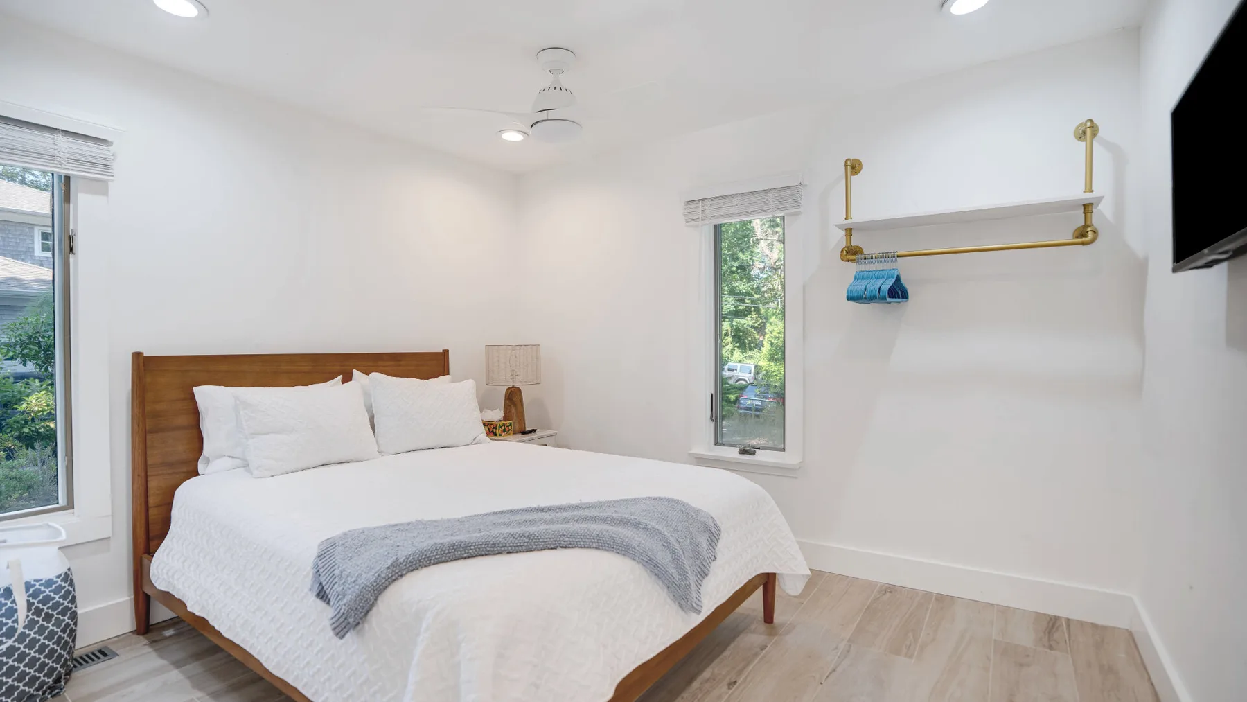 Un dormitorio luminoso con una cama, ropa de cama blanca y ventanas con vistas a la vegetación.