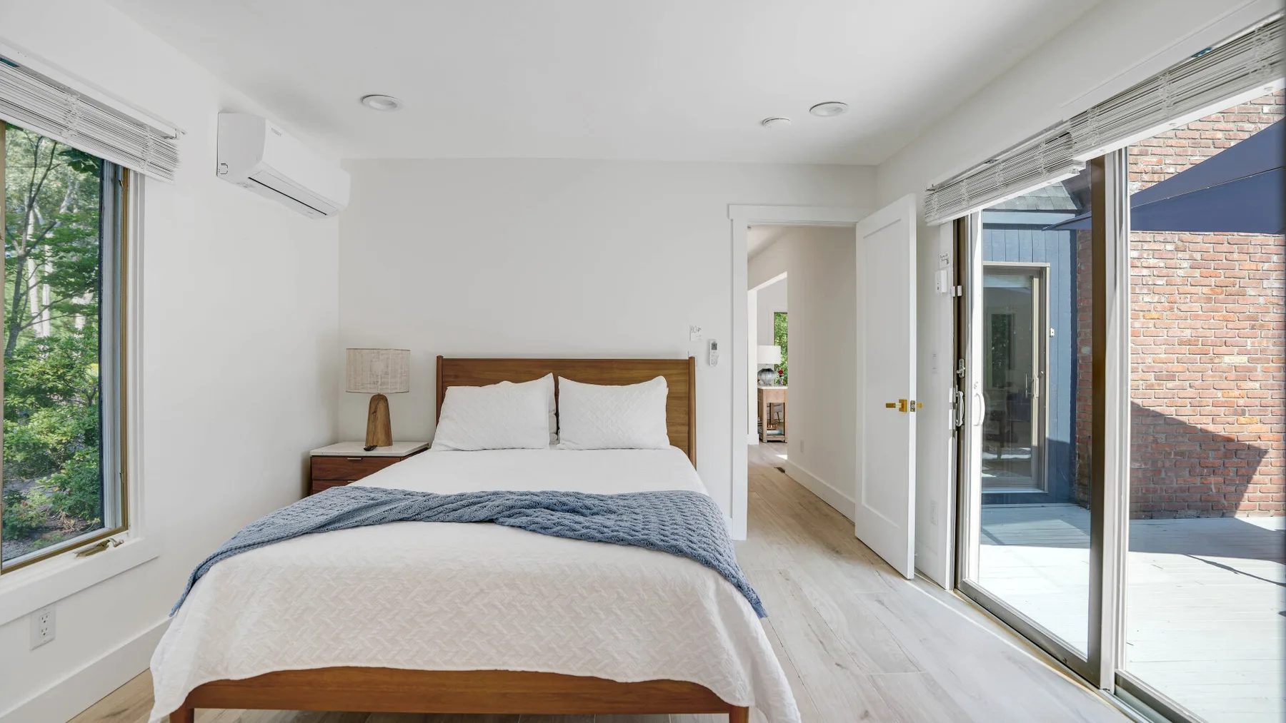 Un dormitorio luminoso con una cama junto a grandes ventanas y puertas corredizas de vidrio.