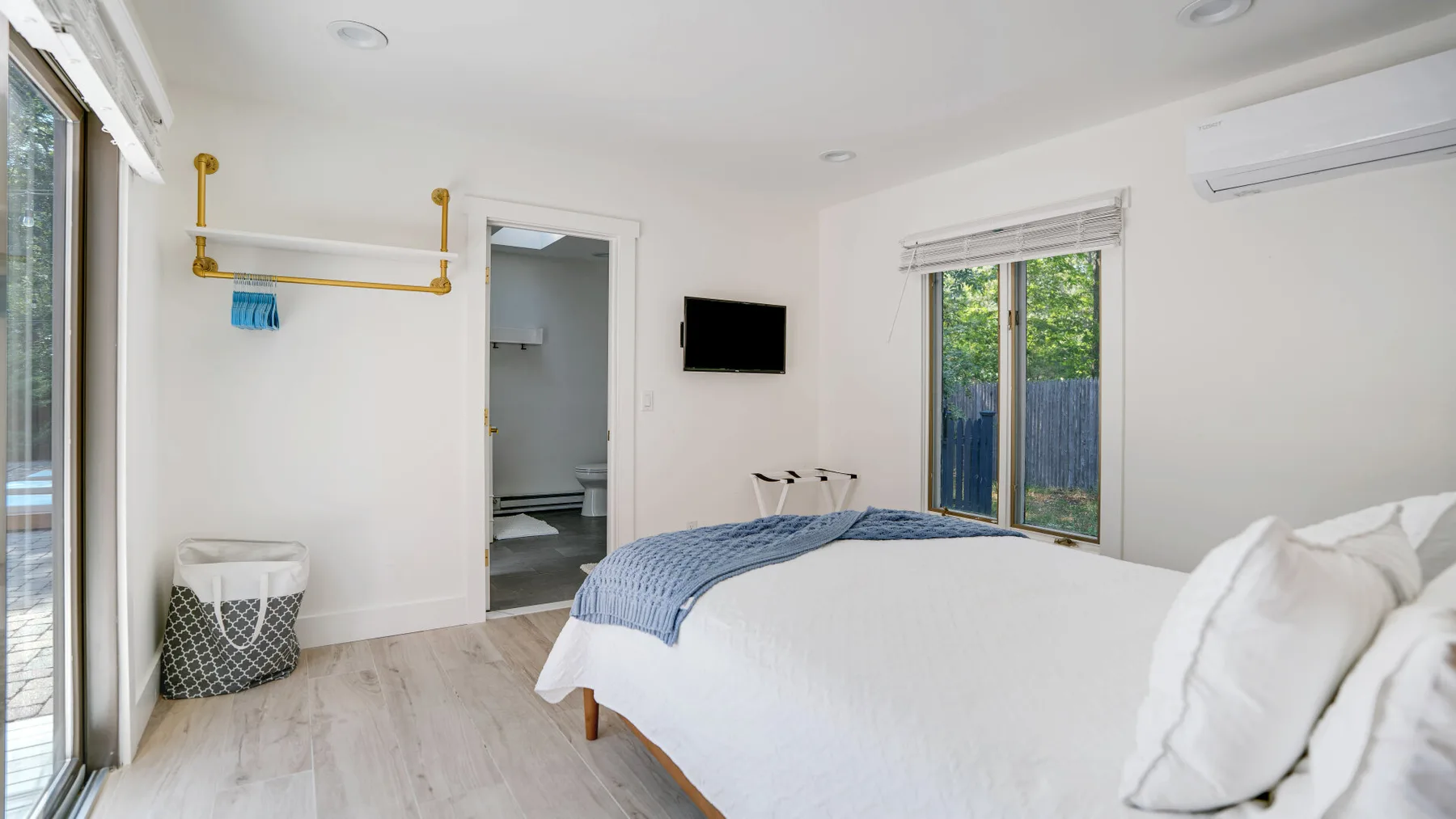Un dormitorio luminoso con una cama tendida y una ventana con vistas a la vegetación.