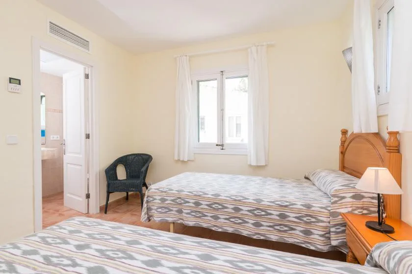 A bedroom with a patterned bed, a window, and a dark woven chair.