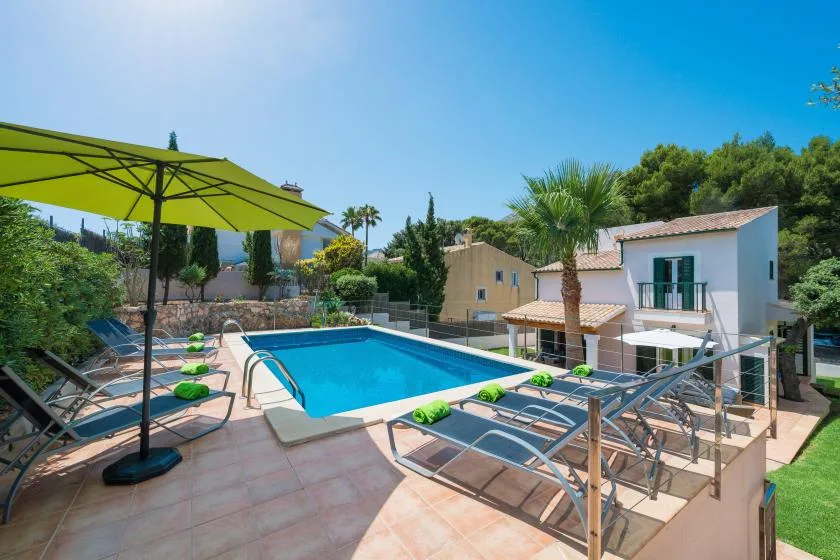 Outdoor swimming pool beside a house, with lounge seating and a large shade umbrella.