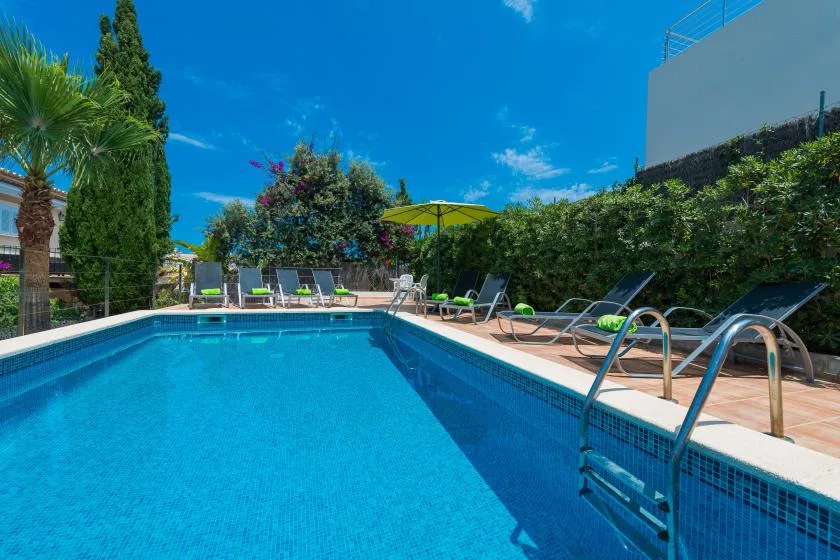 An outdoor swimming pool is surrounded by lounge chairs and greenery.