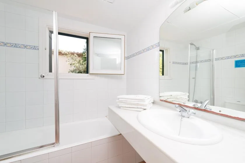 A bright bathroom with a sink, mirror, and tiled shower area.