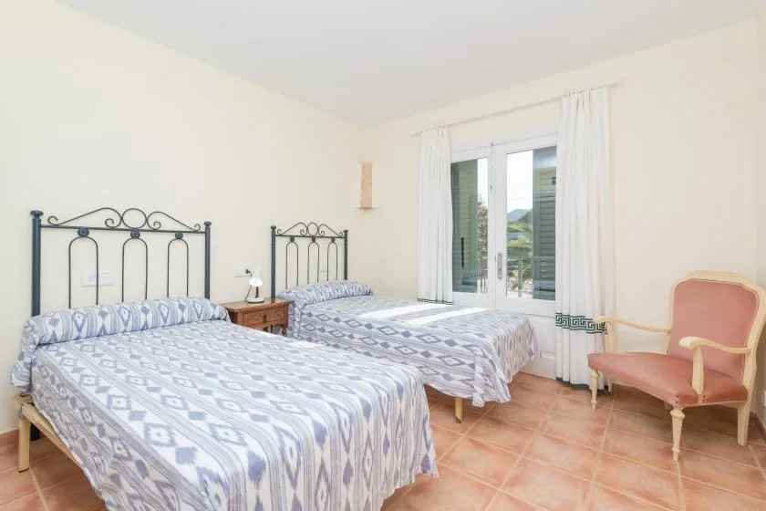 A bright bedroom with two beds and a window overlooking the hills.