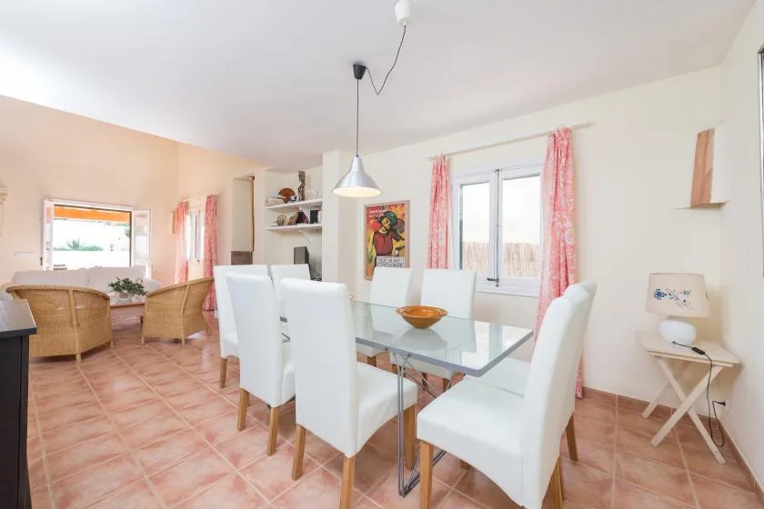 A dining area with a glass table and white seating beside a window.