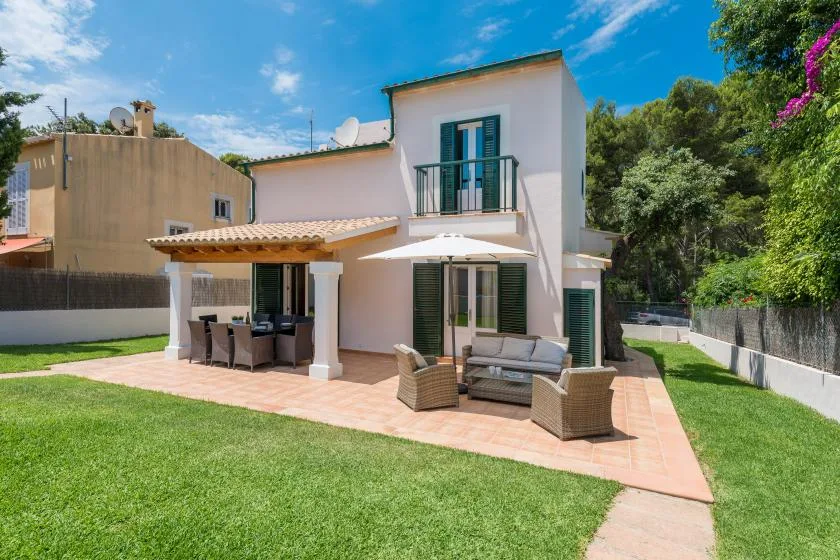 A white two-story house opens onto a tiled patio with outdoor seating and a lawn.