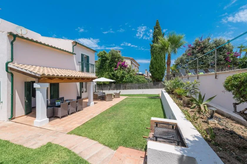 A sunny garden patio with outdoor seating and a rectangular lawn beside a house.