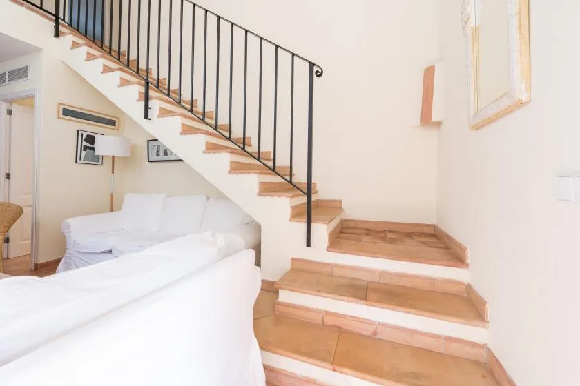 A bright living room with white seating beneath a wooden staircase.