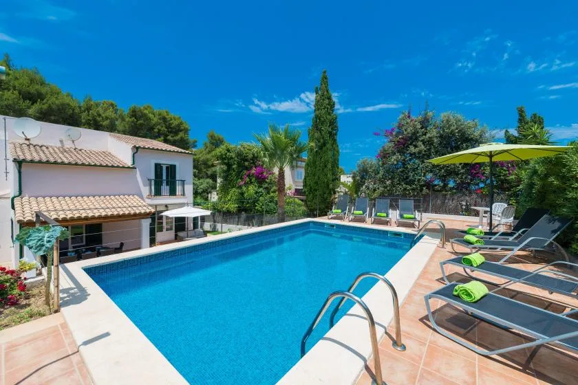 Una piscina exterior junto a una casa, con tumbonas alrededor de la terraza.