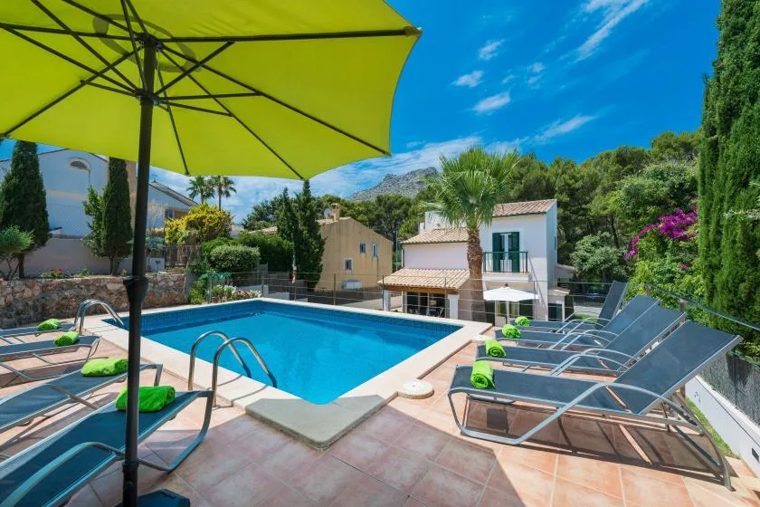 An outdoor swimming pool with lounge seating and a large green umbrella.
