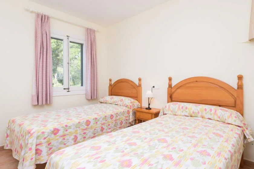 A bedroom with two beds dressed in colorful floral bedding beside a window.