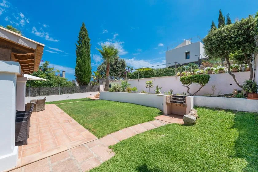 A sunny garden with a lawn, tiled walkway, and raised planting beds.
