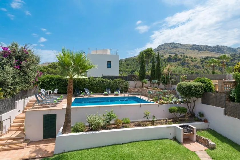 An outdoor swimming pool sits among garden landscaping, with hills in the background.