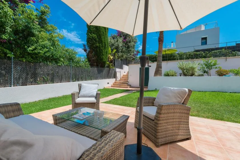 A garden patio with outdoor seating, a glass table, and a large umbrella.