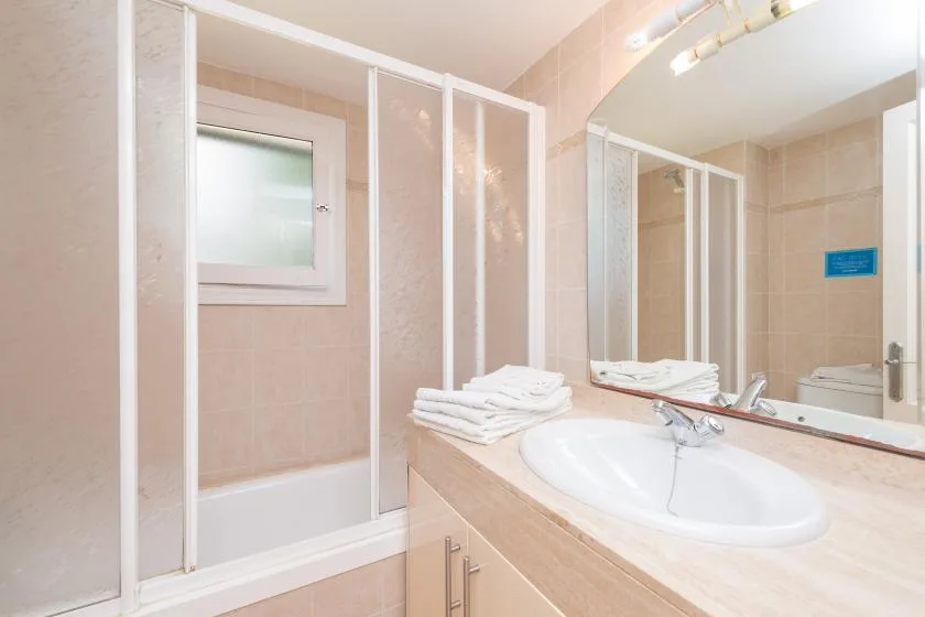 A tiled bathroom with a shower, sink, and folded towels on the counter.