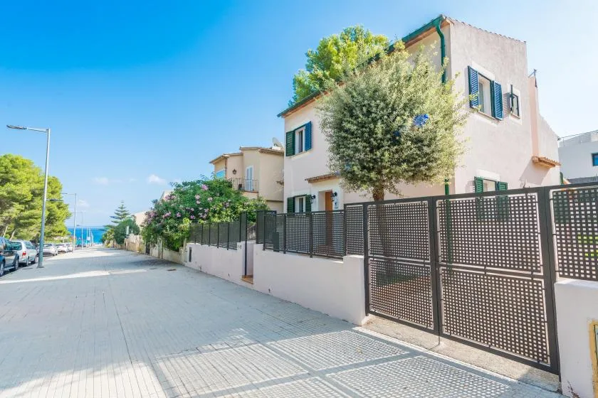 A residential street with a pale house, trees, and a metal fence.
