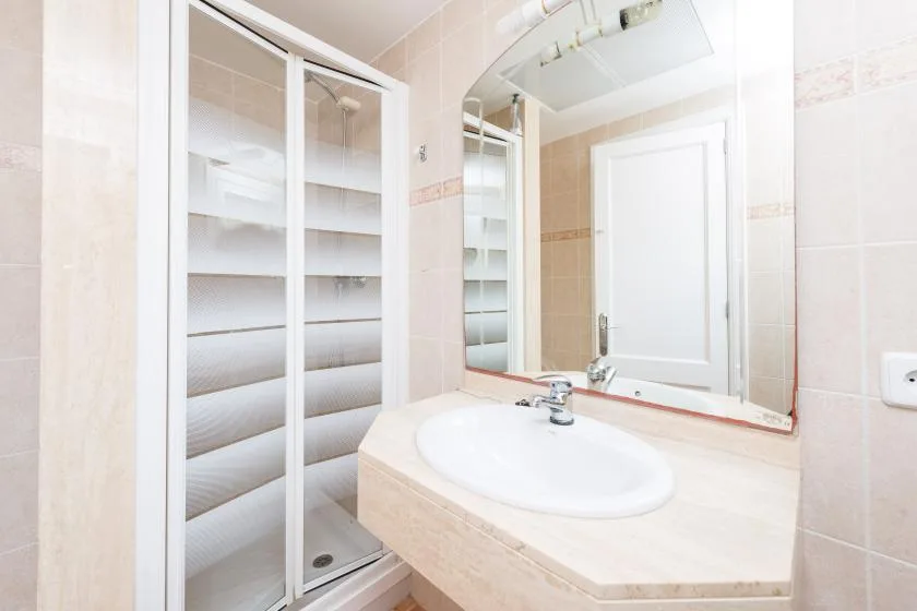 A tiled bathroom with a sink, mirror, and glass shower enclosure.