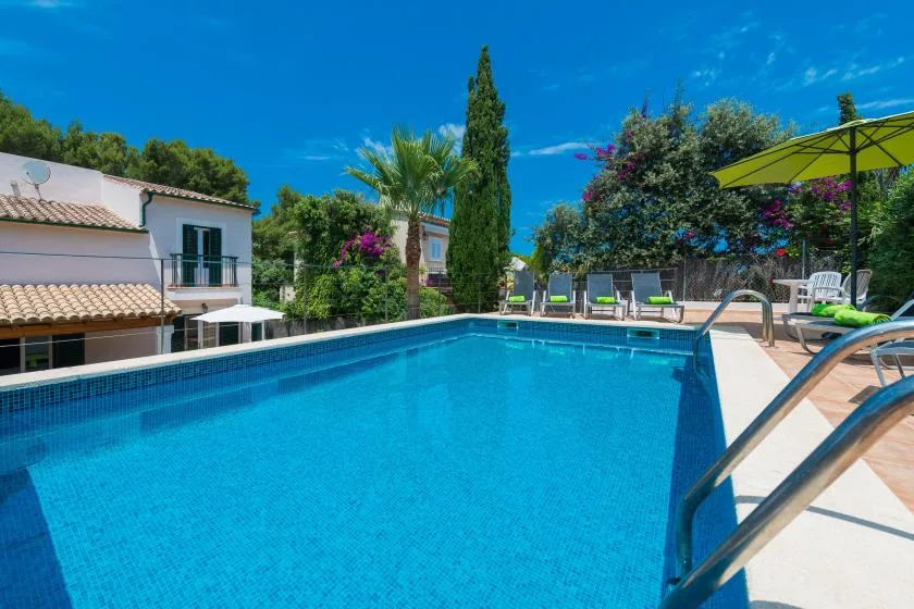 An outdoor swimming pool beside a house, with lounge chairs and greenery.