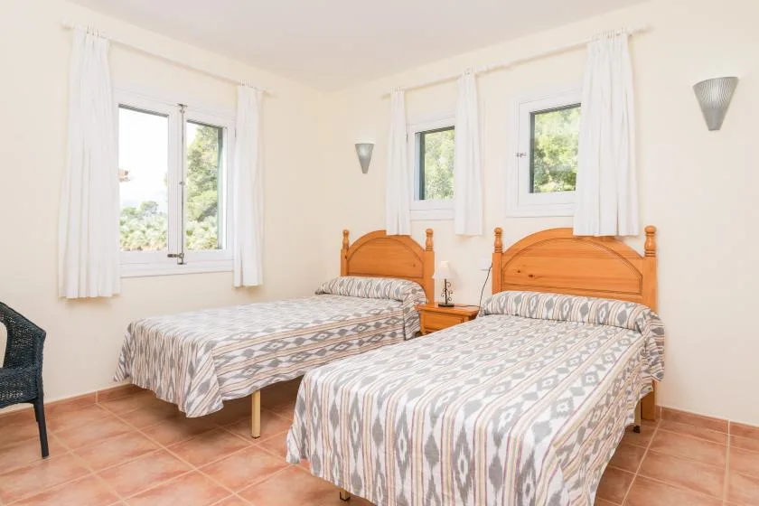 A bright bedroom with two single beds and white curtains.