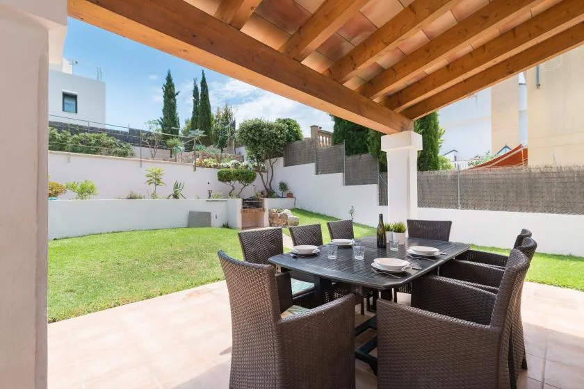 A covered patio dining area with a table and seating beside a lawn.