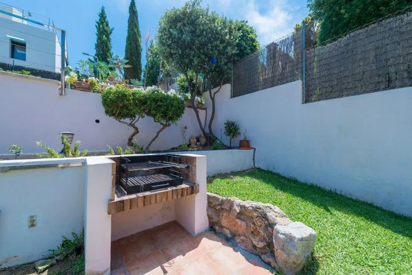 A small outdoor grill stands beside a grassy yard enclosed by white walls.