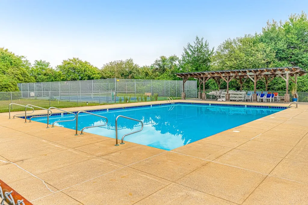 An outdoor swimming pool with a paved deck and a covered seating area.