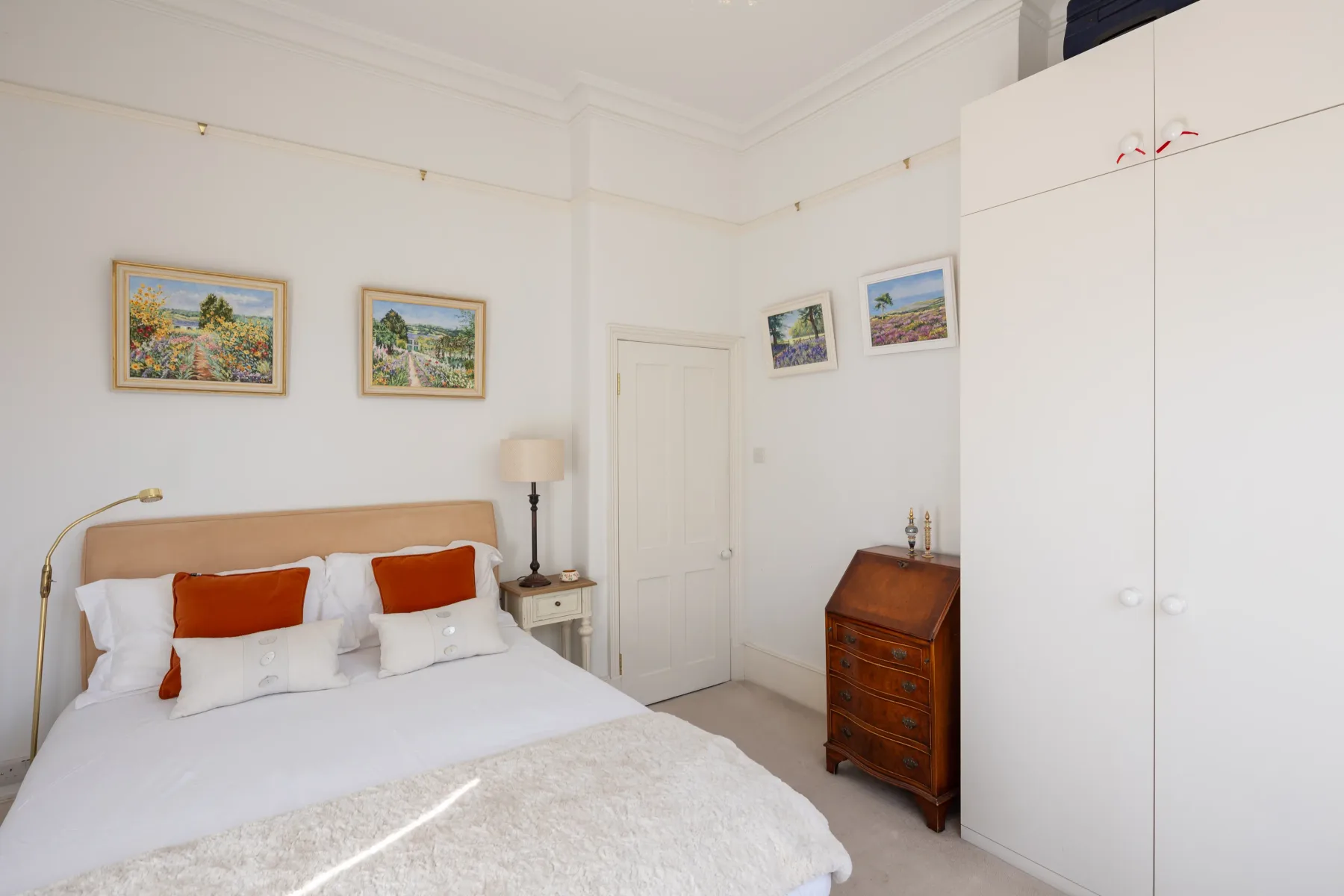 A bright bedroom with a neatly made bed and framed landscape paintings.