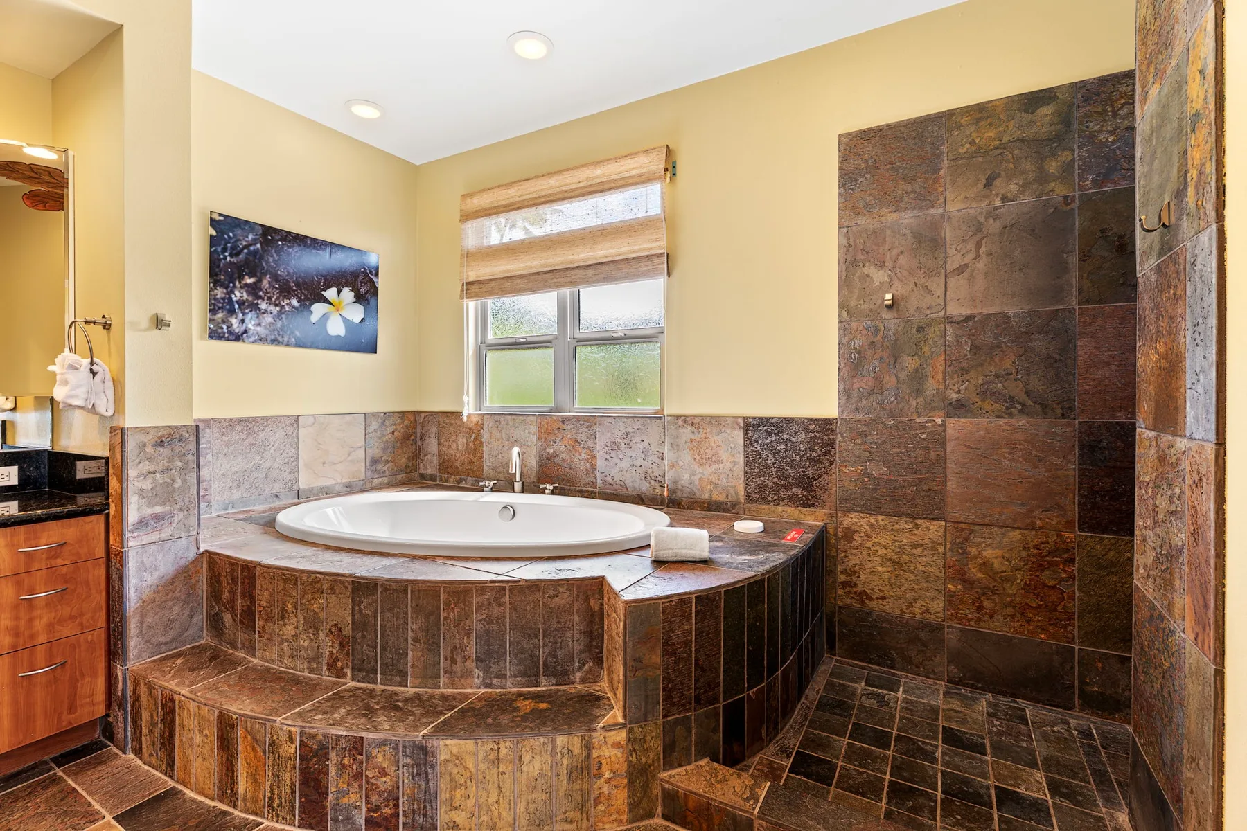 A tiled bathroom with a large corner bathtub beneath a window.