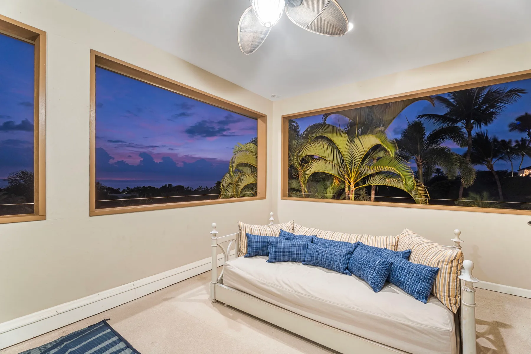 A bedroom with a white bed and blue pillows beside large windows.