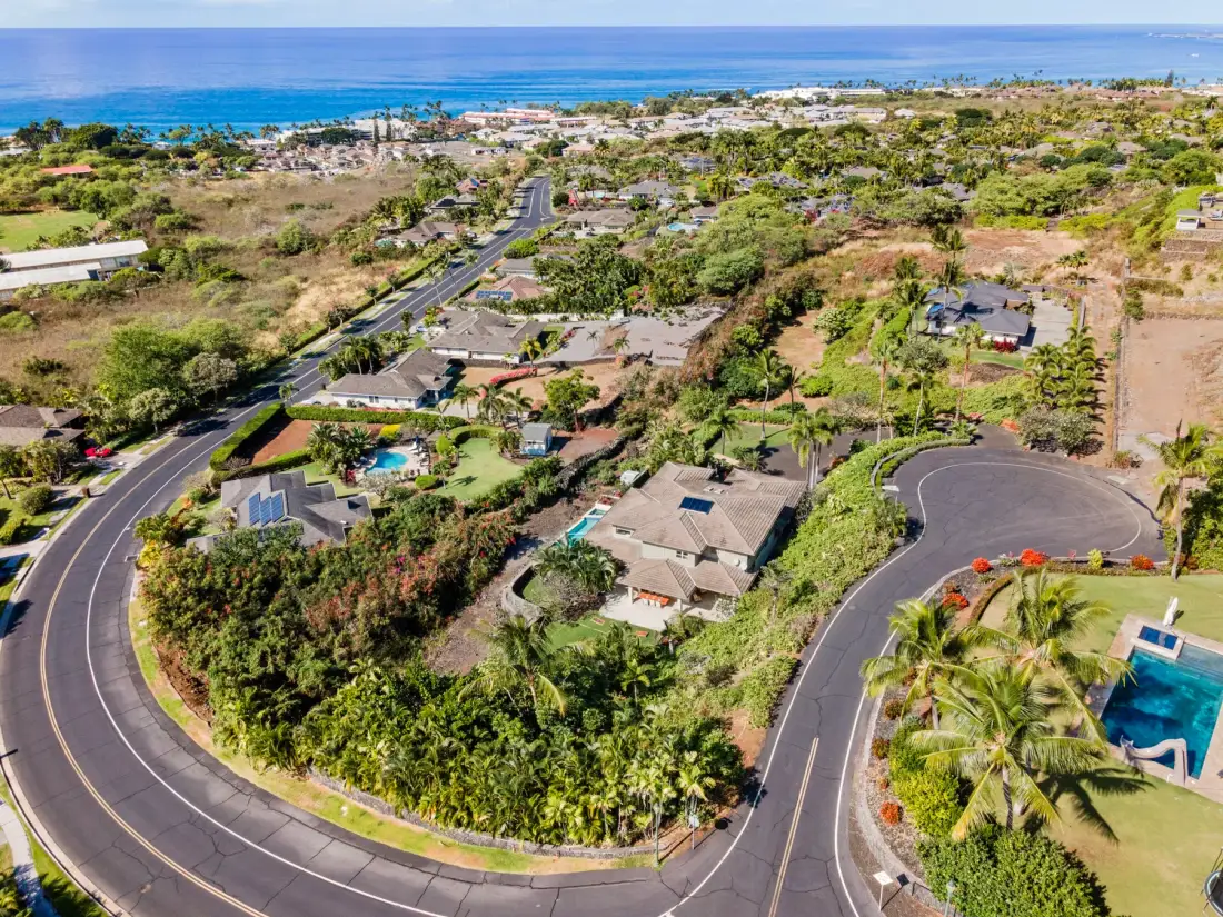 An aerial view of a coastal neighborhood with curved roads and the ocean beyond.