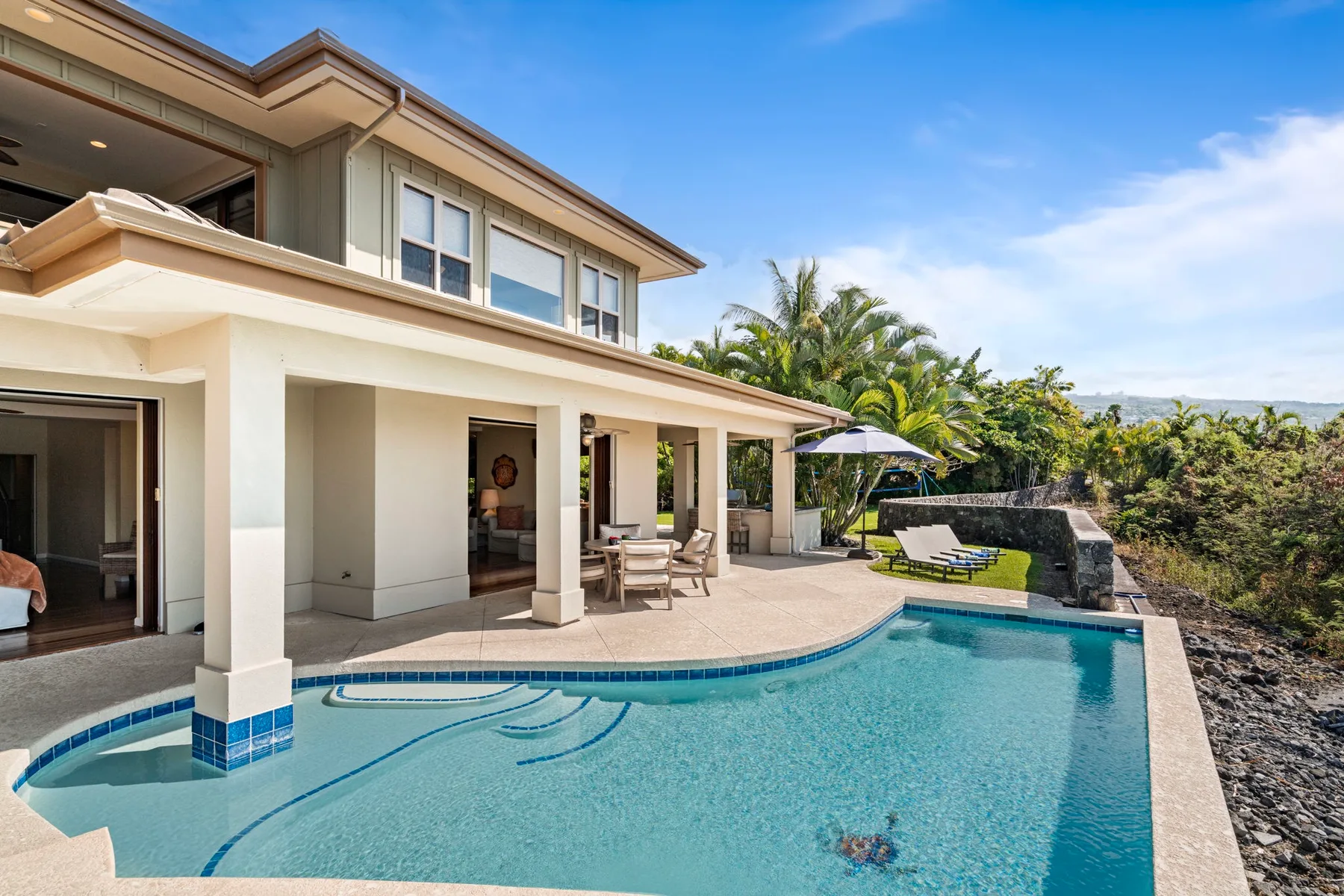 A modern house opens onto a swimming pool, with patio seating beside it.