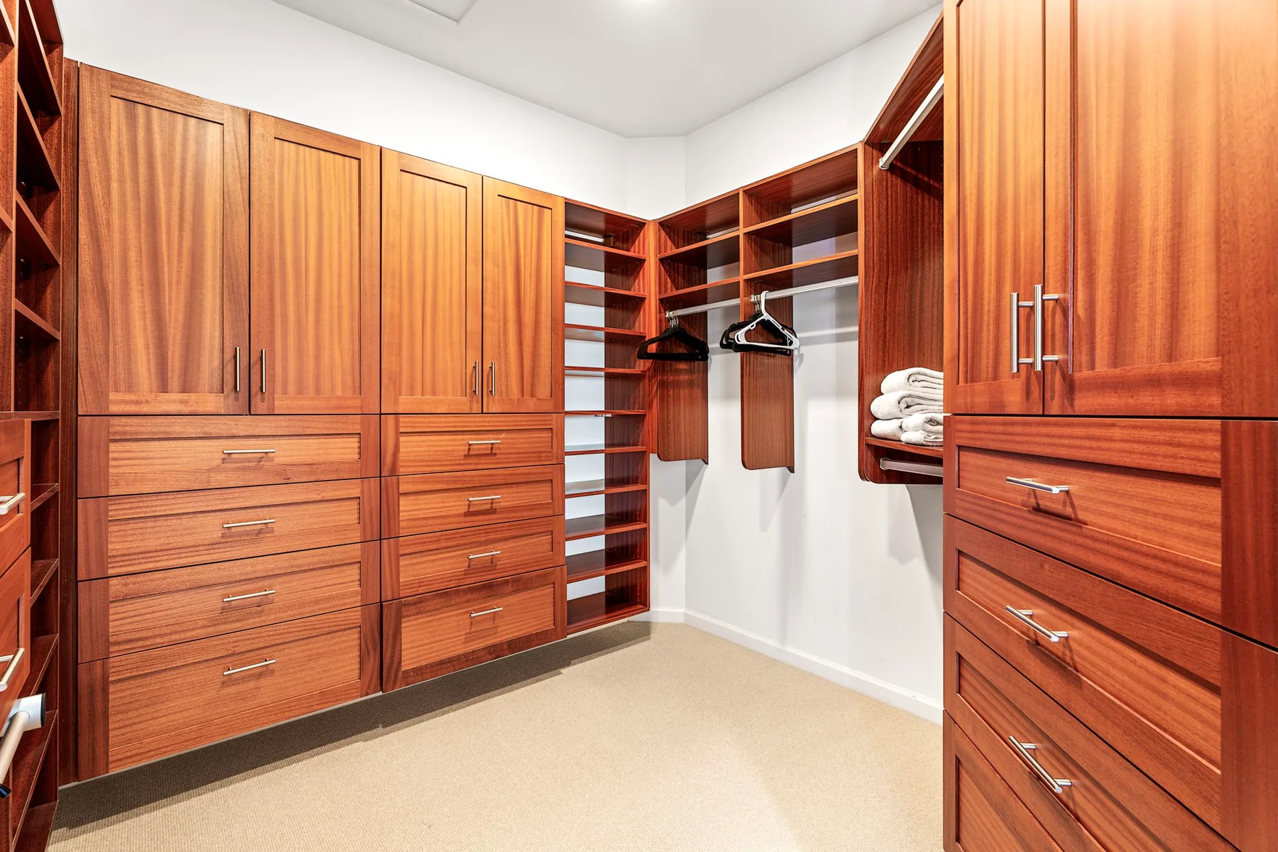 A walk-in closet with wooden cabinetry, drawers, and open shelving.