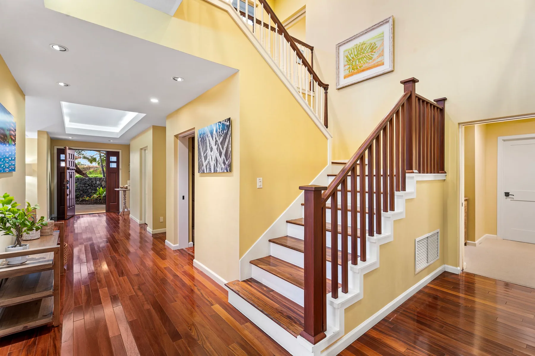 A bright entryway with a wooden staircase and polished wood flooring.