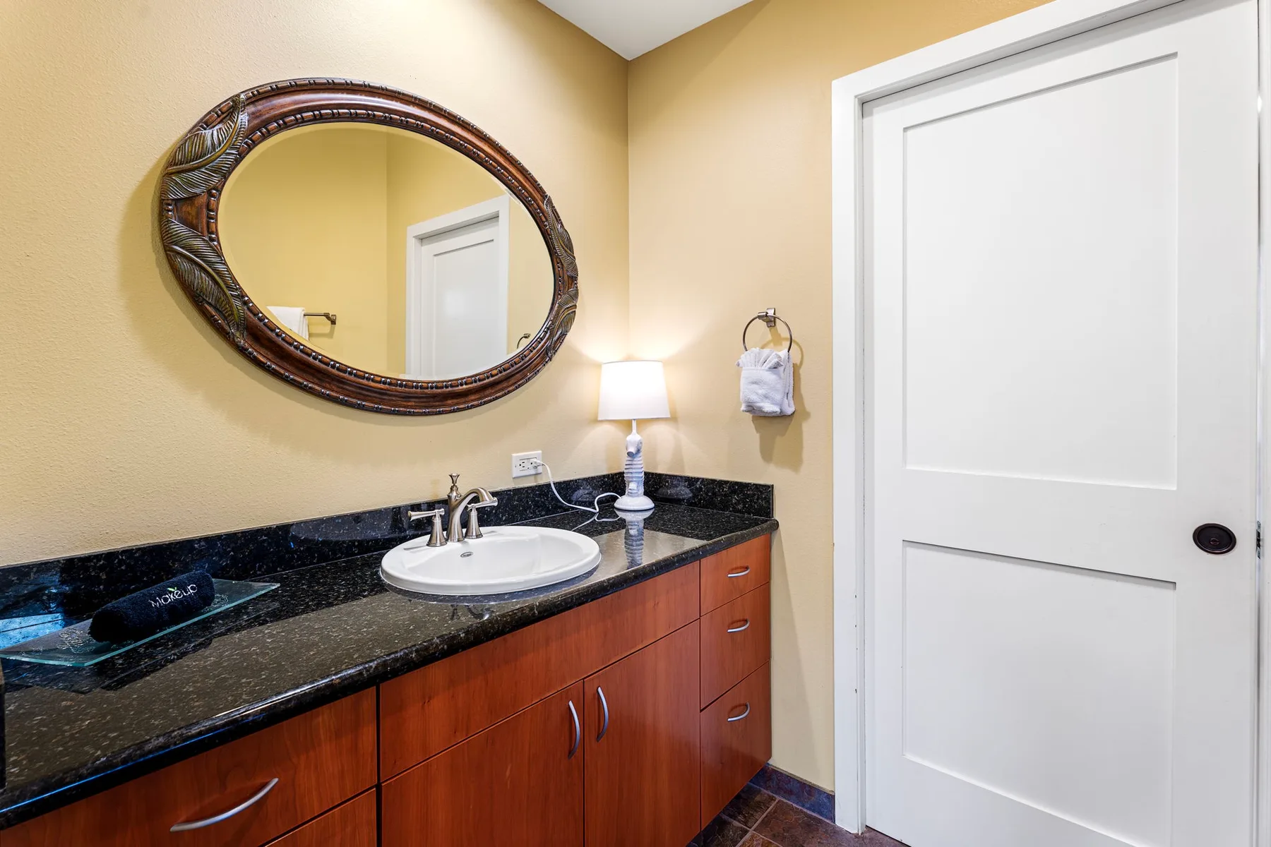 A bathroom vanity with a sink, dark countertop, and oval wall mirror.