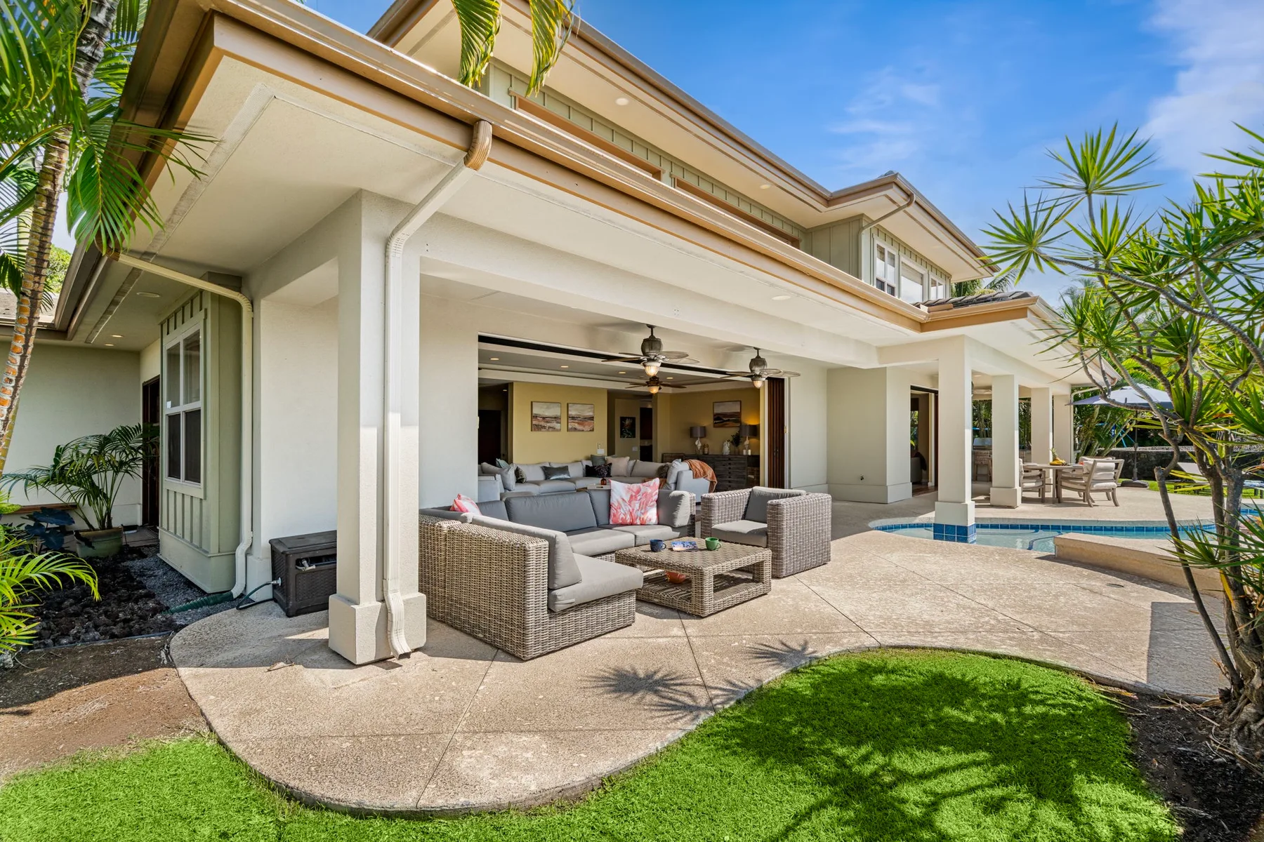 A covered patio with outdoor seating opens onto a pool and lawn.