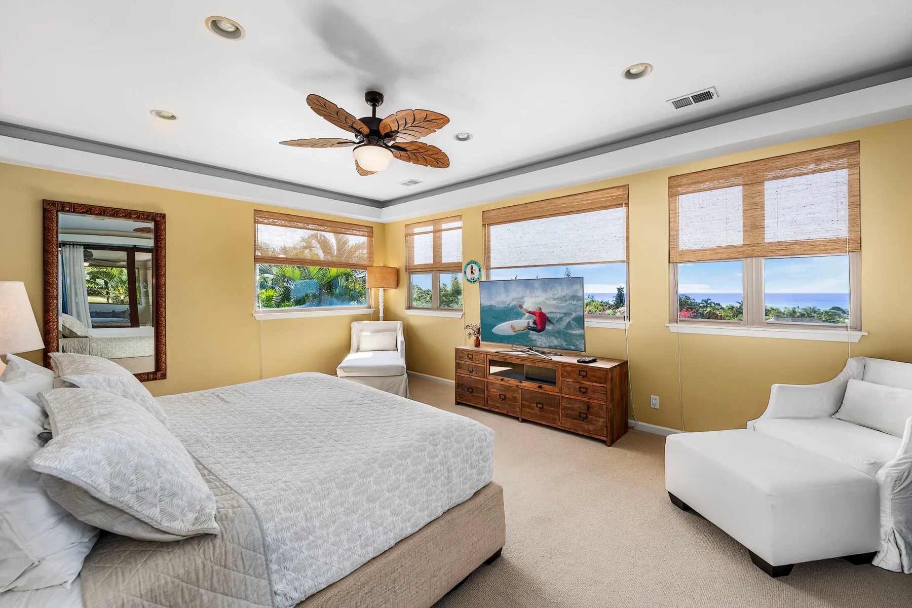 A bright bedroom with a bed, television, and wide windows overlooking the water.