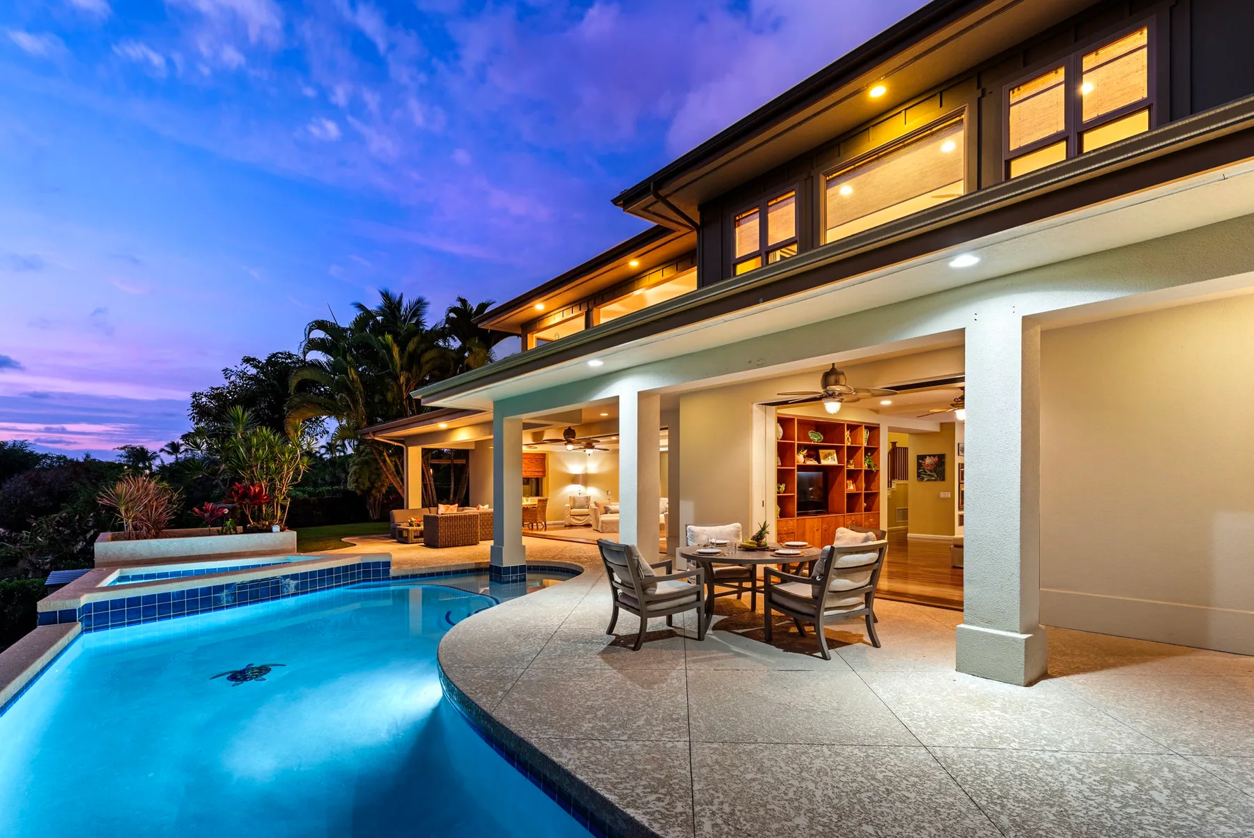 A modern house opens onto a lit patio beside a swimming pool at dusk.