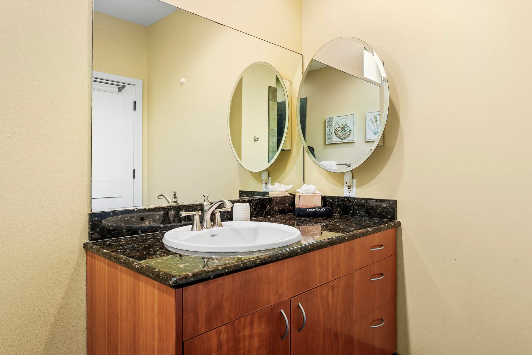 A bathroom vanity with a dark countertop, sink, and round mirrors.