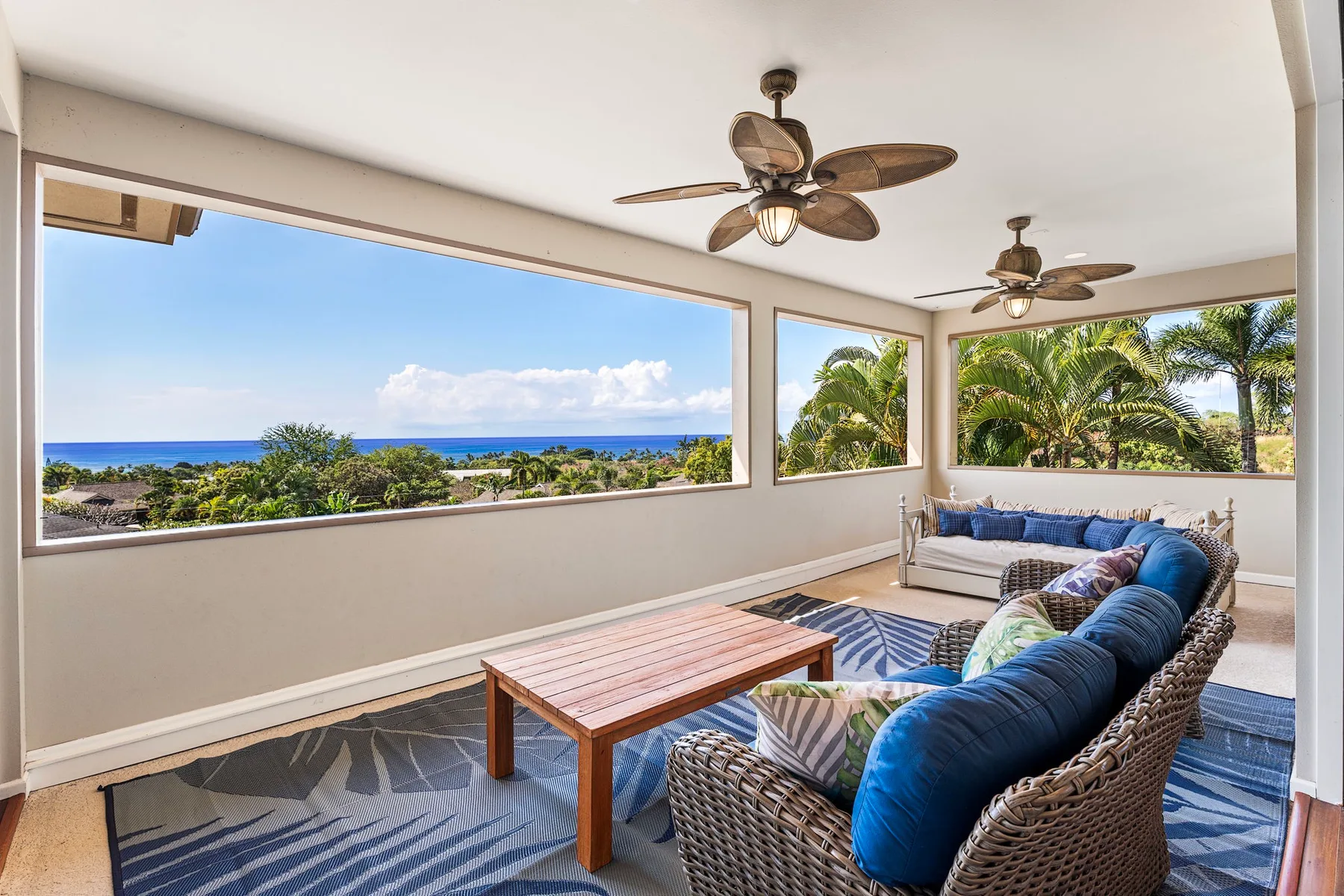A bright living room with broad windows overlooking the ocean and palm trees.