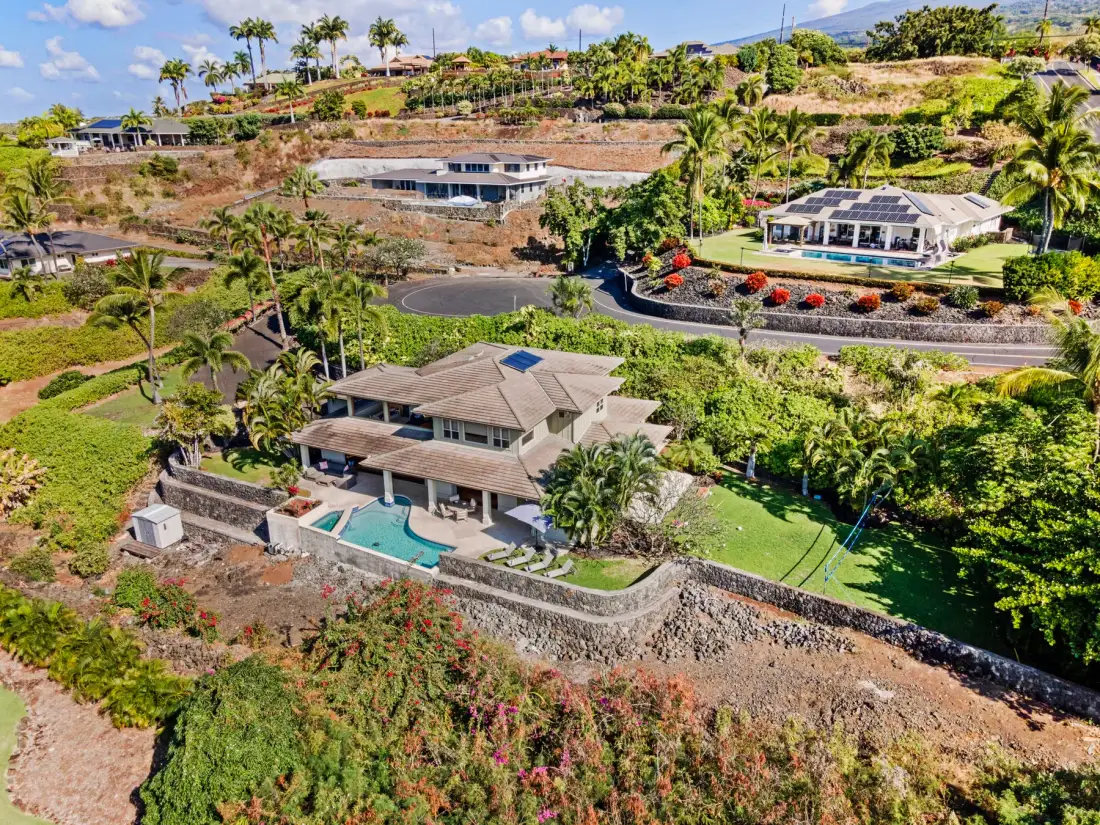 Aerial view of a hillside residential area with homes, roads, and tropical greenery.