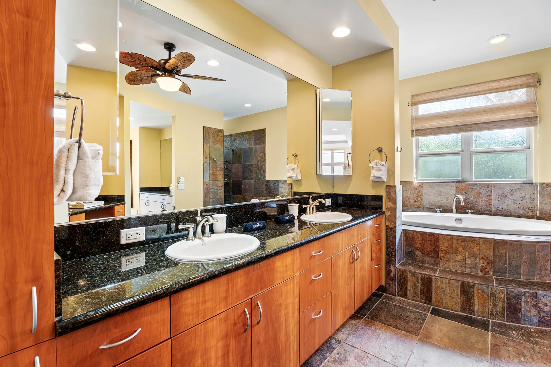 A bathroom vanity with two sinks faces a tiled bathtub beneath a window.