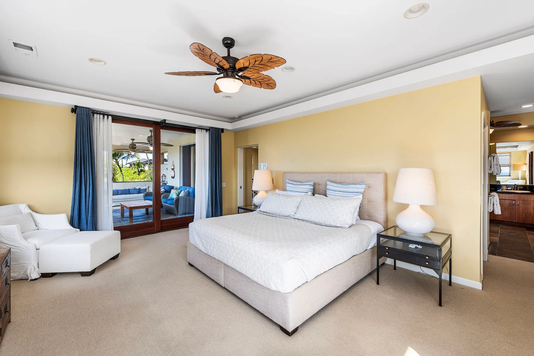 A bright bedroom with a large bed and a white seating area beside glass doors.